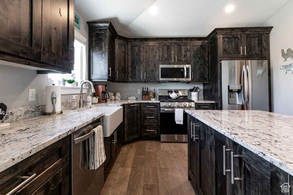 Kitchen with stainless steel appliances, dark wood-style flooring, light stone countertops, dark brown cabinetry, and recessed lighting