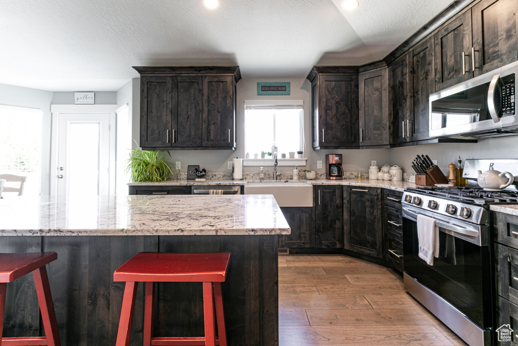 Kitchen featuring appliances with stainless steel finishes, wood finished floors, a kitchen bar, light stone counters, and recessed lighting