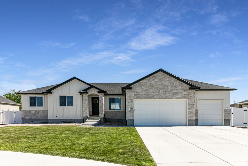 View of front of property with an attached garage, concrete driveway, a gate, board and batten siding, and stone siding