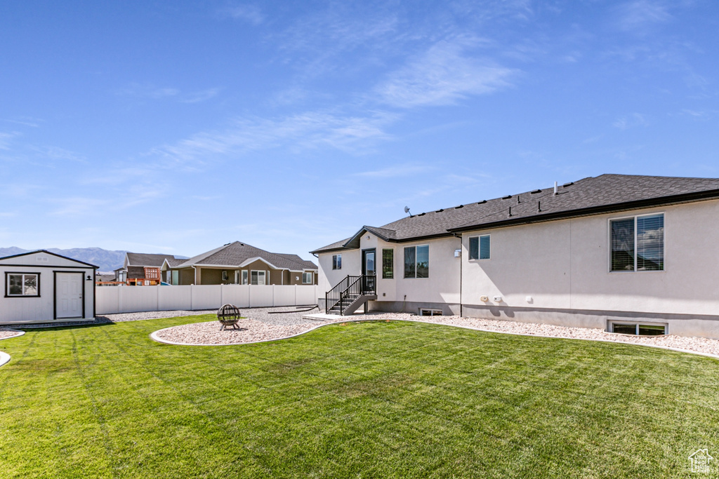 Back of house with a fenced backyard, an outdoor fire pit, a shed, a shingled roof, and stucco siding