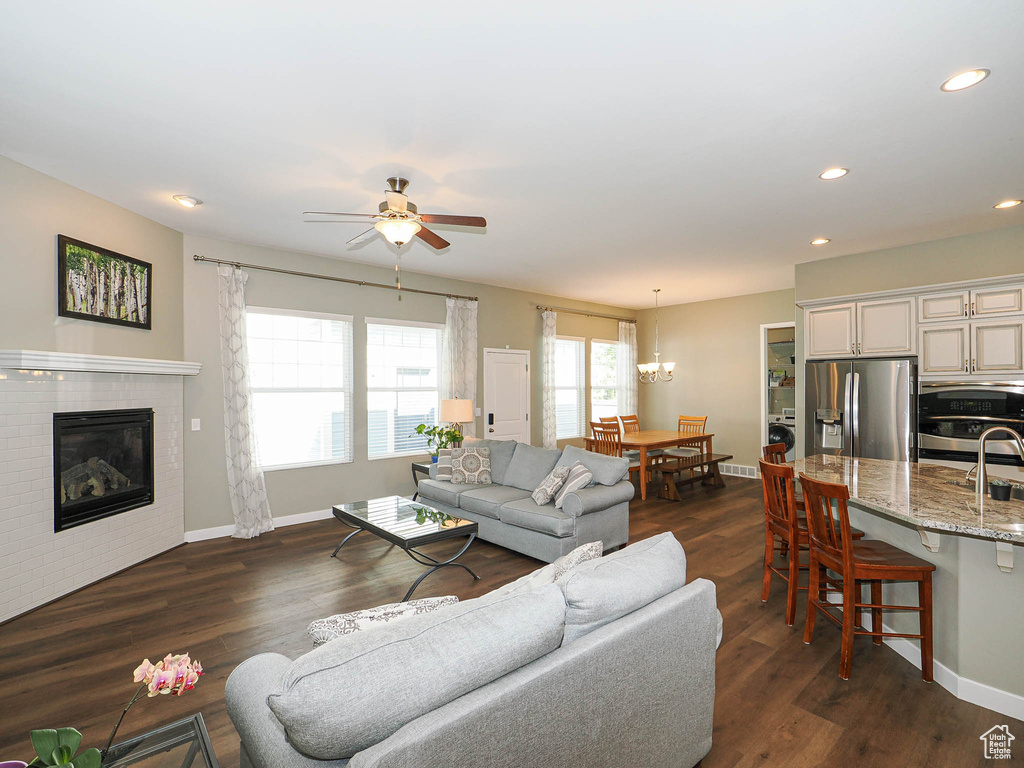 Living area featuring a ceiling fan, recessed lighting, a brick fireplace, a chandelier, and dark wood-type flooring
