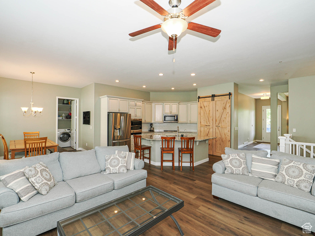 Living area with washer / dryer, a barn door, a chandelier, dark wood-type flooring, and a ceiling fan