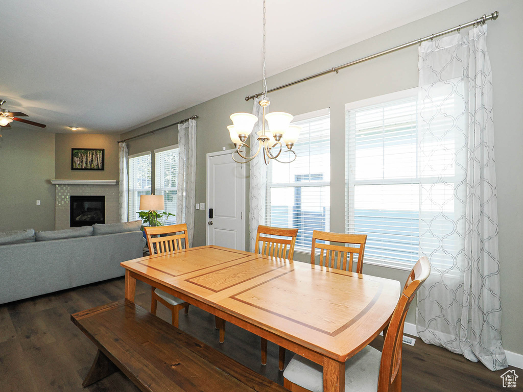 Dining area featuring dark wood-type flooring, a chandelier, a glass covered fireplace, and a ceiling fan