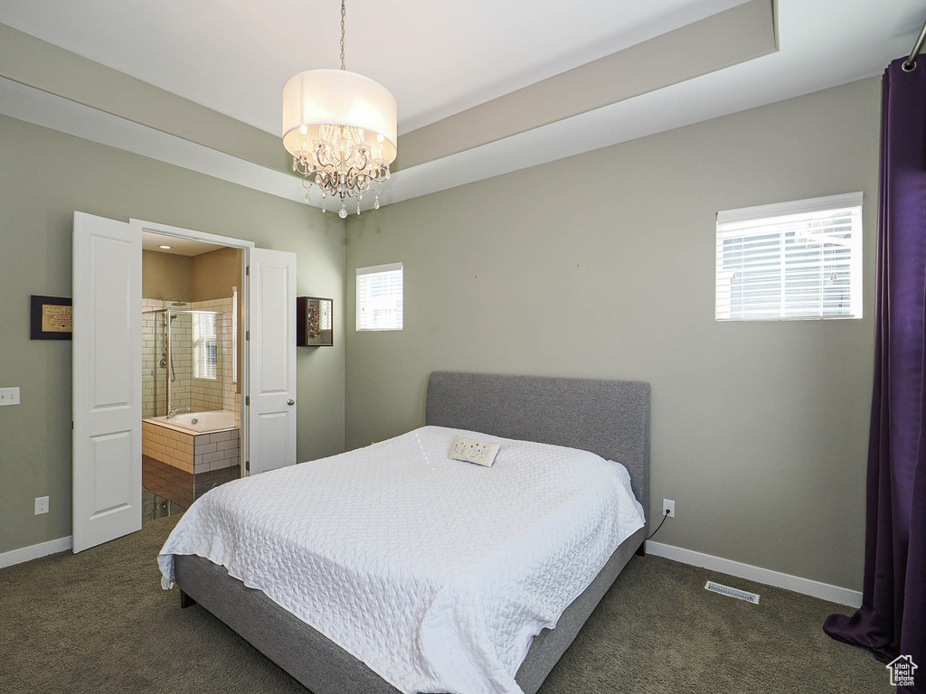 Bedroom featuring dark carpet, a chandelier, connected bathroom, and a raised ceiling