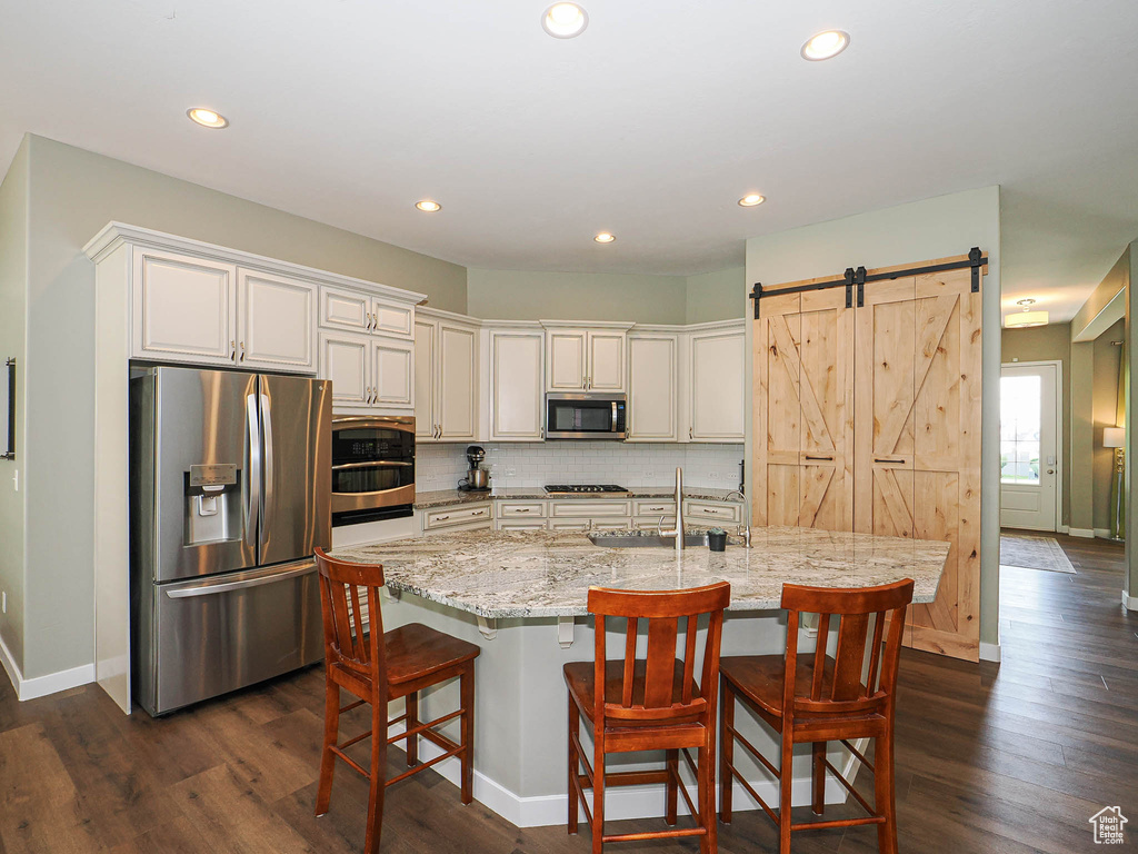 Kitchen featuring stainless steel appliances, recessed lighting, light stone countertops, decorative backsplash, and dark wood-style floors