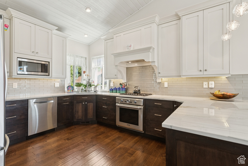 Kitchen featuring appliances with stainless steel finishes, vaulted ceiling, white cabinetry, dark brown cabinets, and dark wood-style flooring