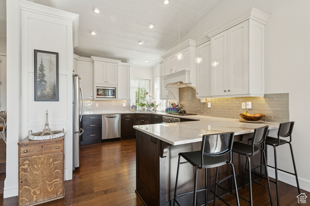 Kitchen with appliances with stainless steel finishes, a peninsula, white cabinets, dark wood finished floors, and decorative backsplash