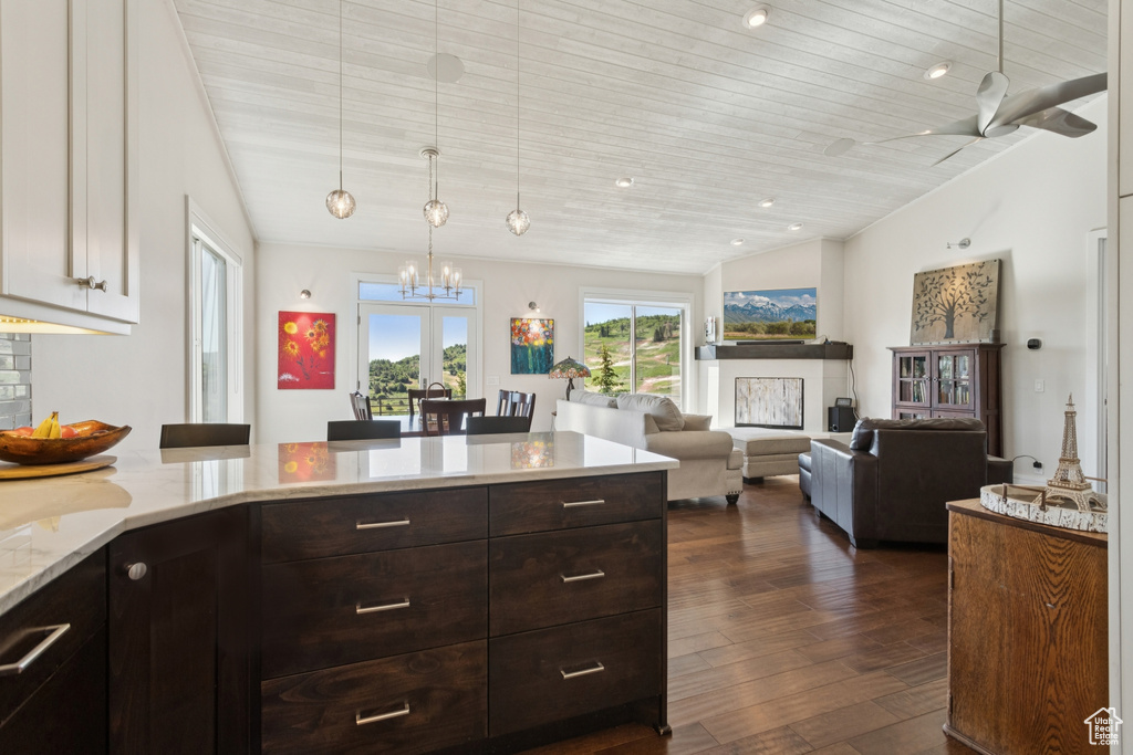 Kitchen with a chandelier, dark wood-type flooring, vaulted ceiling, dark brown cabinetry, and light stone countertops