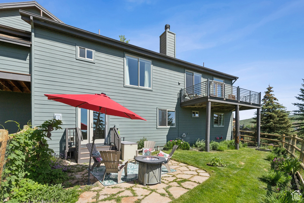 Back of property featuring a balcony, an outdoor fire pit, a chimney, and a patio area