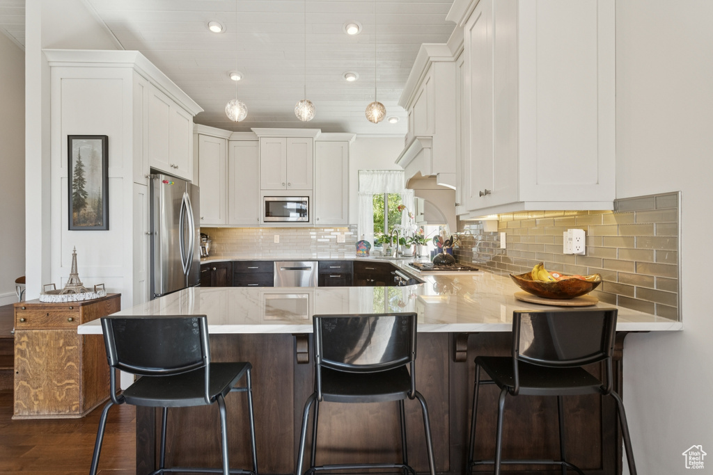 Kitchen featuring appliances with stainless steel finishes, a peninsula, white cabinetry, dark wood-style floors, and recessed lighting