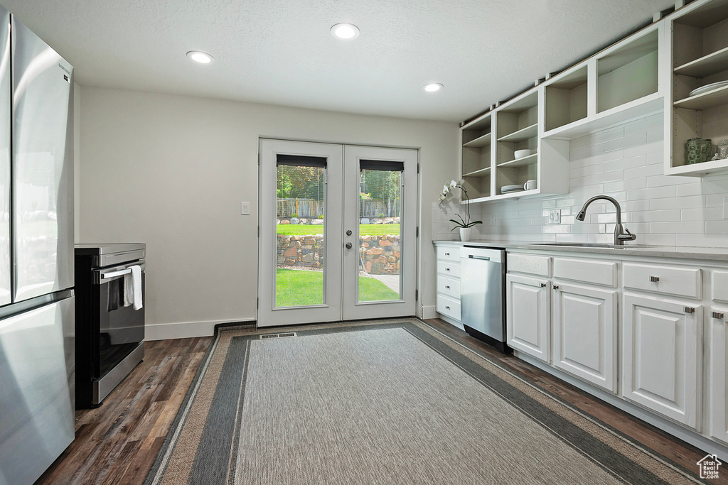 Kitchen with stainless steel appliances, open shelves, dark wood-style flooring, white cabinetry, and french doors