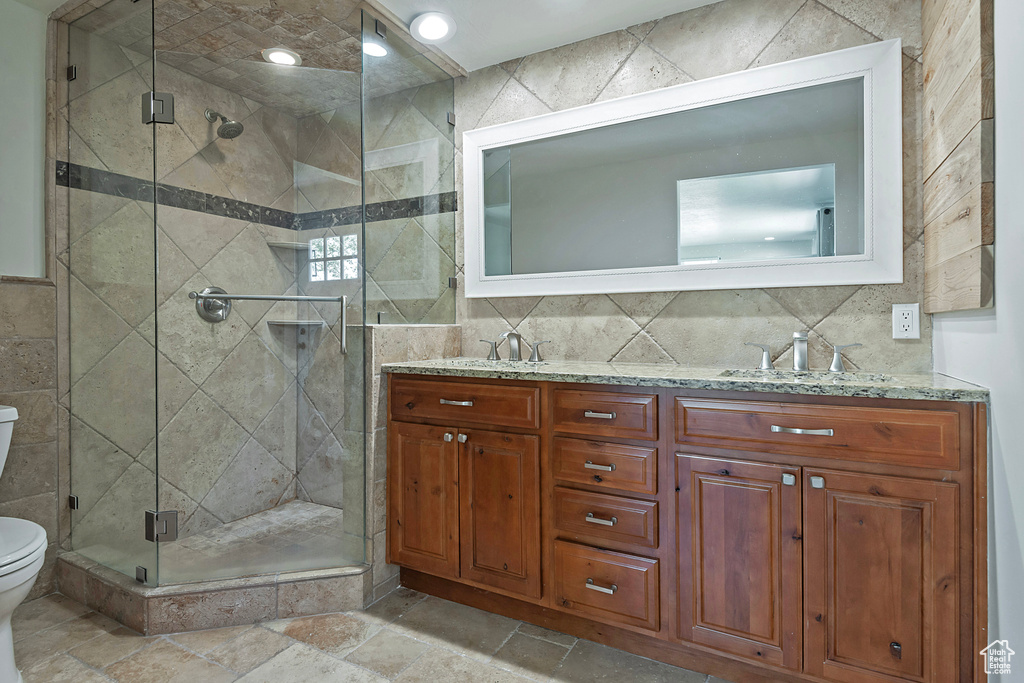 Full bath featuring tile walls, double vanity, a stall shower, and stone tile flooring