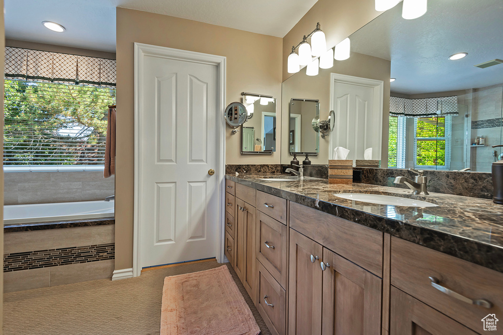 Full bath with double vanity, a relaxing tiled tub, and recessed lighting