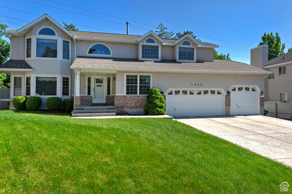 View of front facade featuring an attached garage, driveway, stucco siding, a front lawn, and brick siding