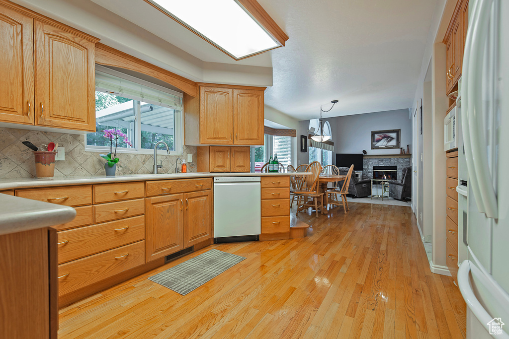 Kitchen with white appliances, light wood-style floors, decorative backsplash, a glass covered fireplace, and light countertops