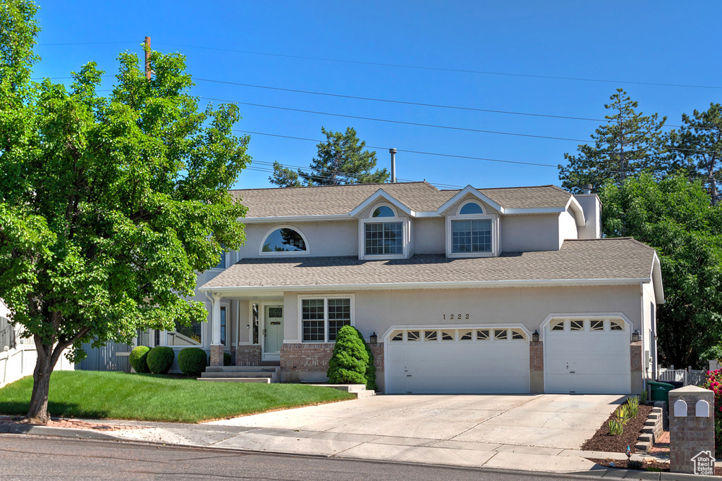Traditional home with driveway, stucco siding, a front lawn, an attached garage, and brick siding