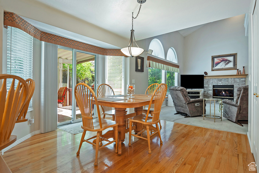 Dining area with light wood-style floors, a glass covered fireplace, and vaulted ceiling