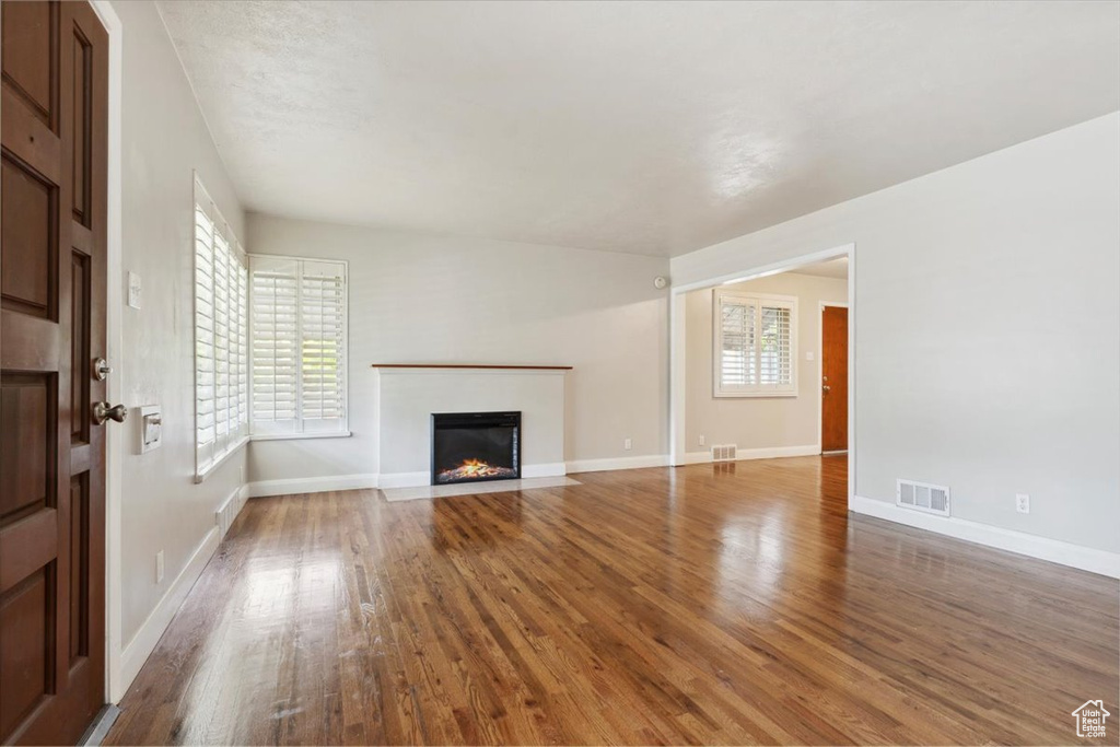 Unfurnished living room with wood finished floors, a fireplace with flush hearth, and plenty of natural light