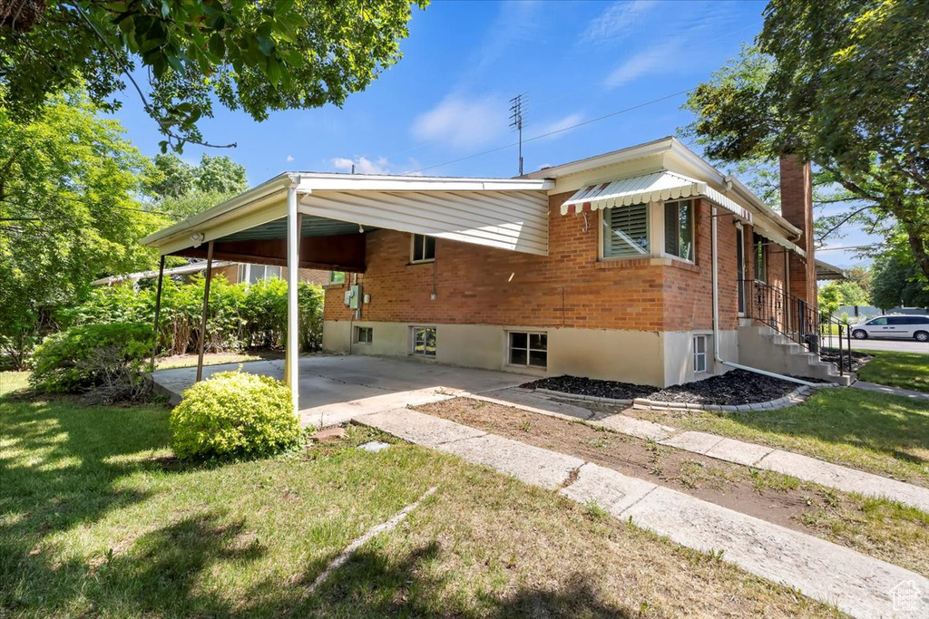Rear view of house featuring brick siding, a carport, a yard, and driveway