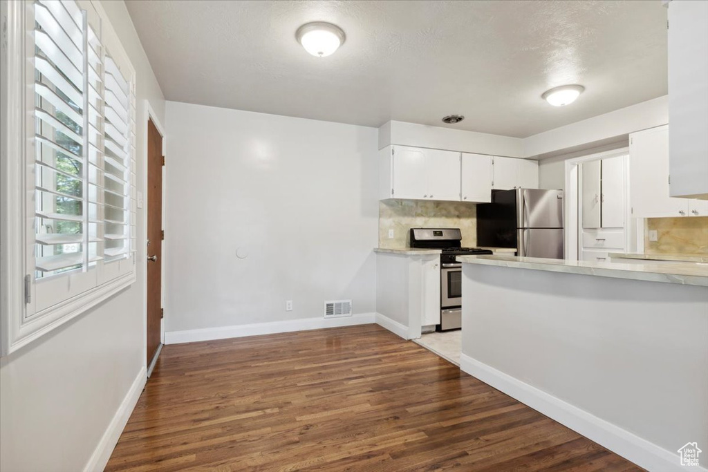 Kitchen featuring stainless steel appliances, light countertops, wood finished floors, white cabinetry, and tasteful backsplash