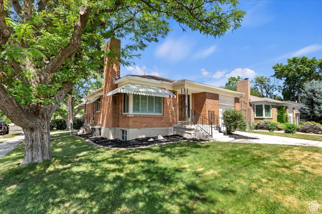 Ranch-style house with brick siding, a chimney, a garage, and a front yard