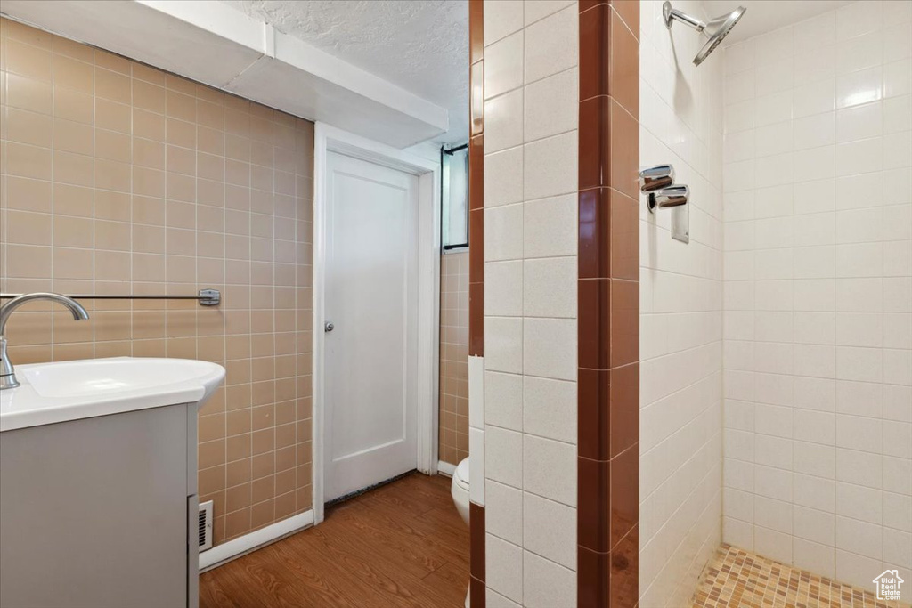 Full bath featuring tile walls, wood finished floors, vanity, and a stall shower