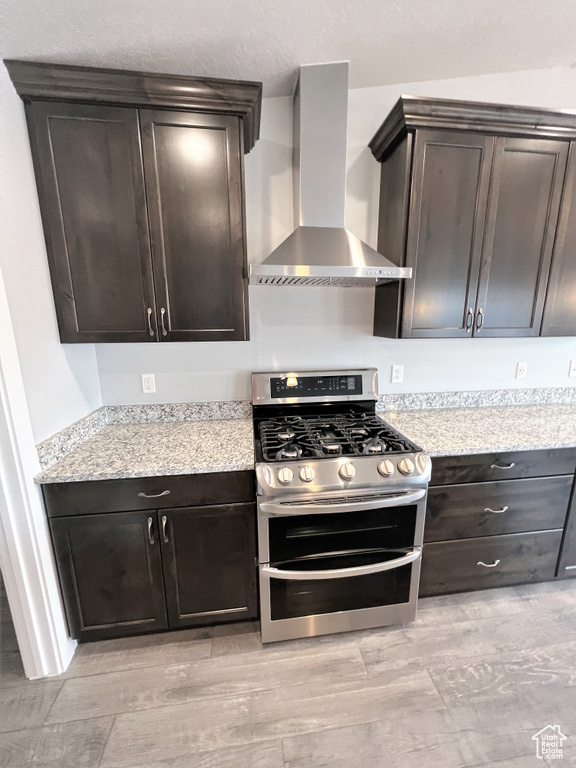 Kitchen featuring range with two ovens, wall chimney exhaust hood, dark brown cabinetry, and light wood-style flooring