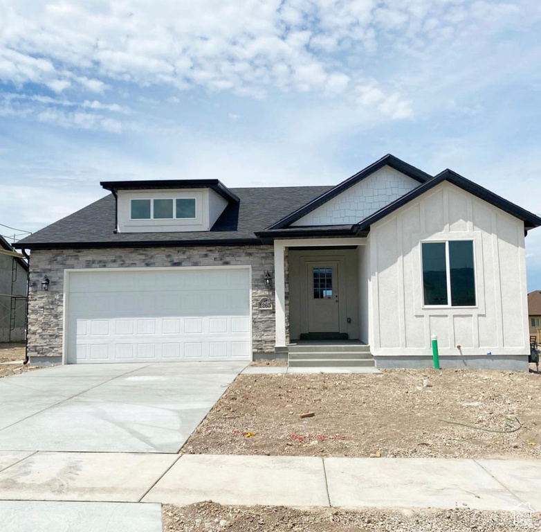 View of front of house featuring concrete driveway, an attached garage, and stone siding