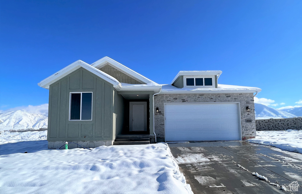 View of front facade with driveway, board and batten siding, an attached garage, a mountain view, and stone siding