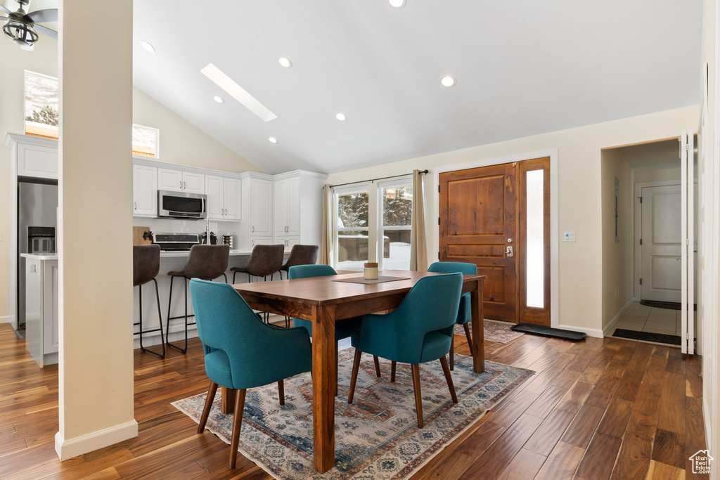 Dining space featuring dark wood-type flooring, a skylight, high vaulted ceiling, and recessed lighting