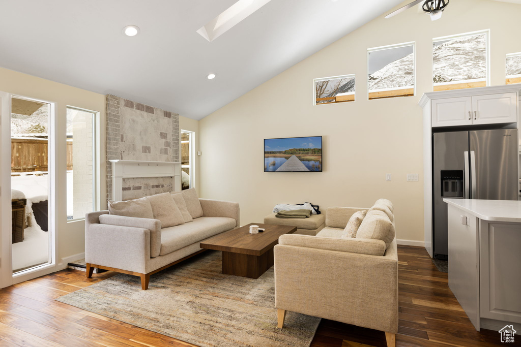 Living area with dark wood-type flooring, recessed lighting, a fireplace, high vaulted ceiling, and a skylight