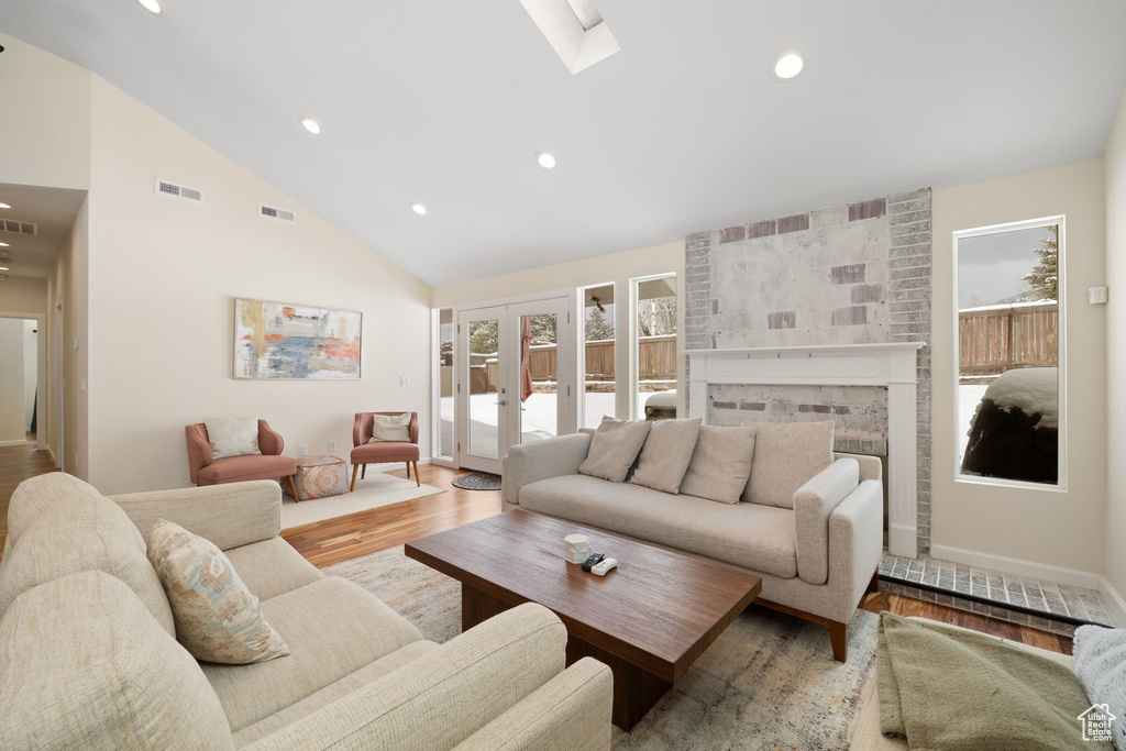 Living room with wood finished floors, recessed lighting, high vaulted ceiling, a skylight, and a fireplace