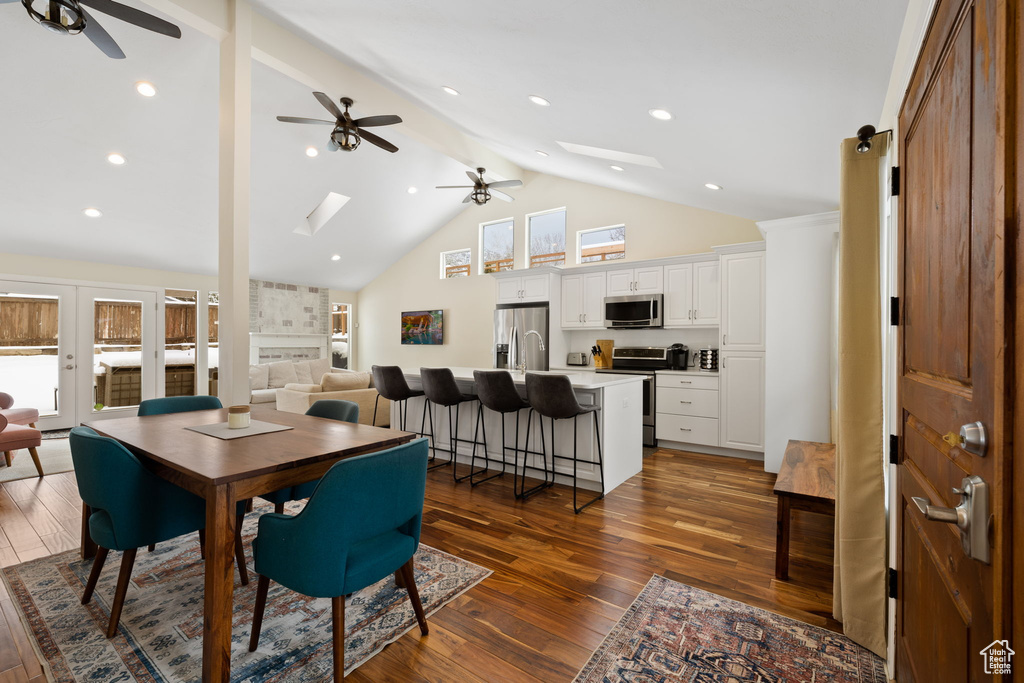 Dining area with a ceiling fan, a skylight, dark wood finished floors, beam ceiling, and high vaulted ceiling