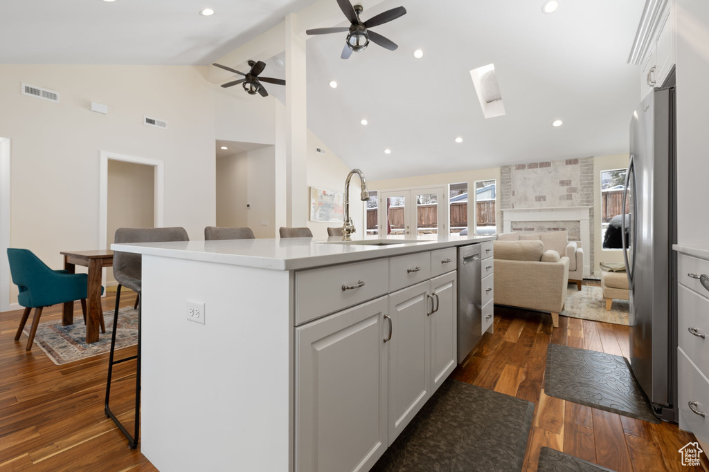 Kitchen featuring open floor plan, appliances with stainless steel finishes, dark wood finished floors, a skylight, and a center island with sink