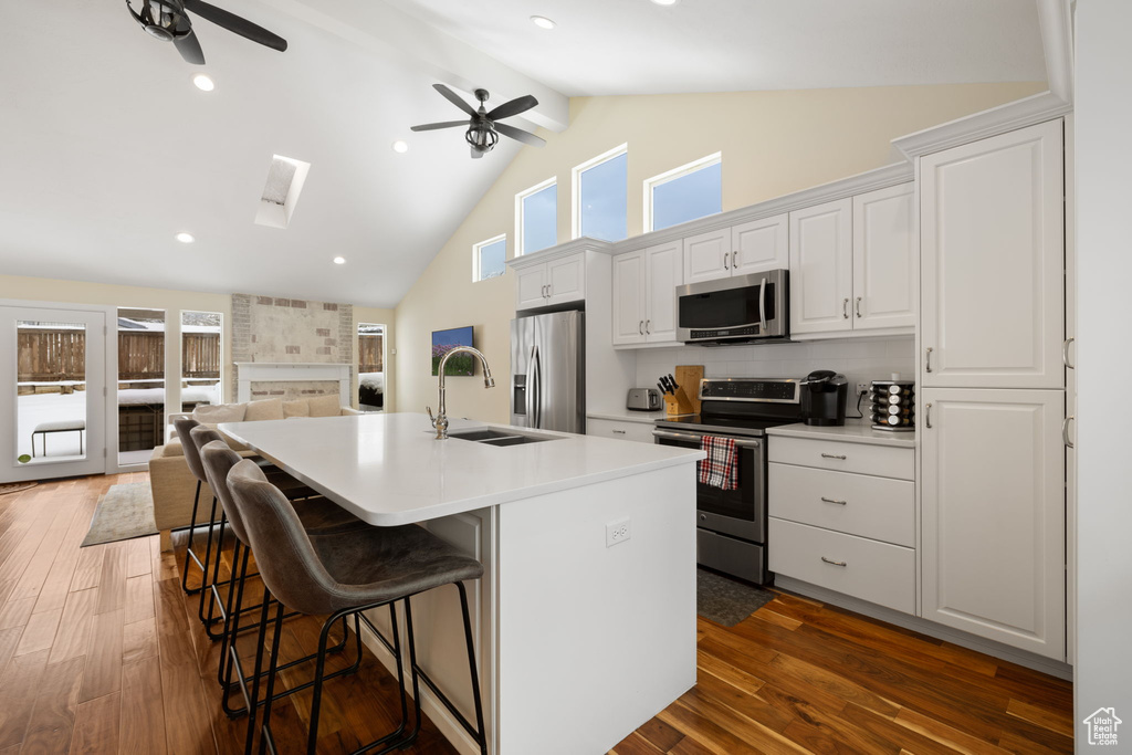 Kitchen featuring appliances with stainless steel finishes, a ceiling fan, a center island with sink, high vaulted ceiling, and a breakfast bar