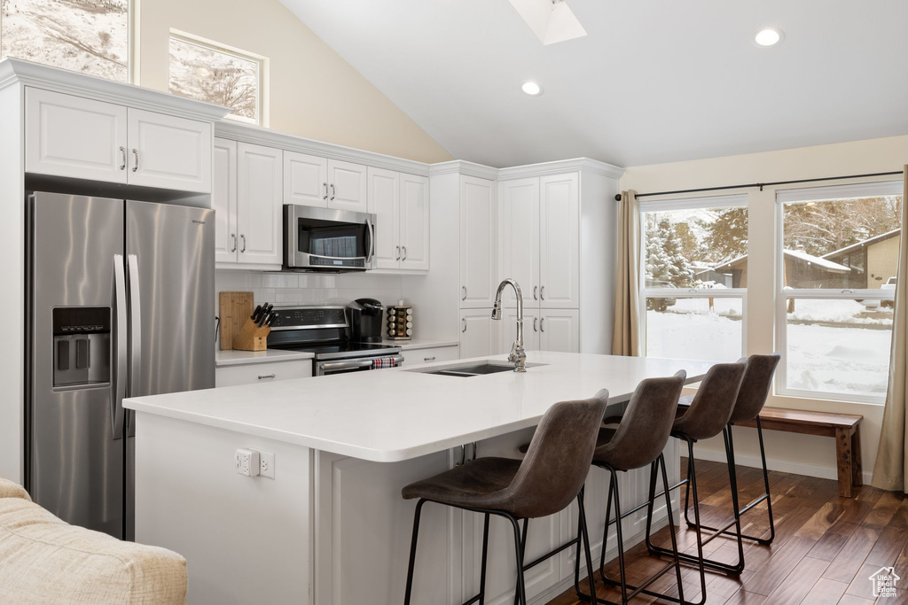 Kitchen with appliances with stainless steel finishes, white cabinets, a skylight, backsplash, and lofted ceiling