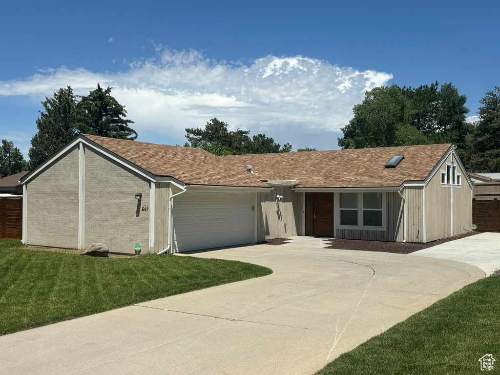 Ranch-style home with concrete driveway, a garage, a front yard, and roof with shingles