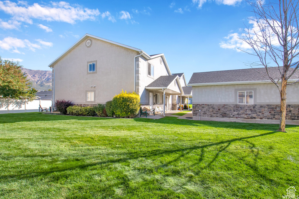 Back of property featuring stucco siding, a yard, a porch, and stone siding