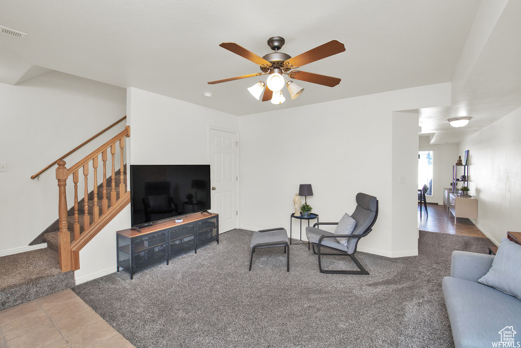 Living room with carpet, stairs, a ceiling fan, and baseboards