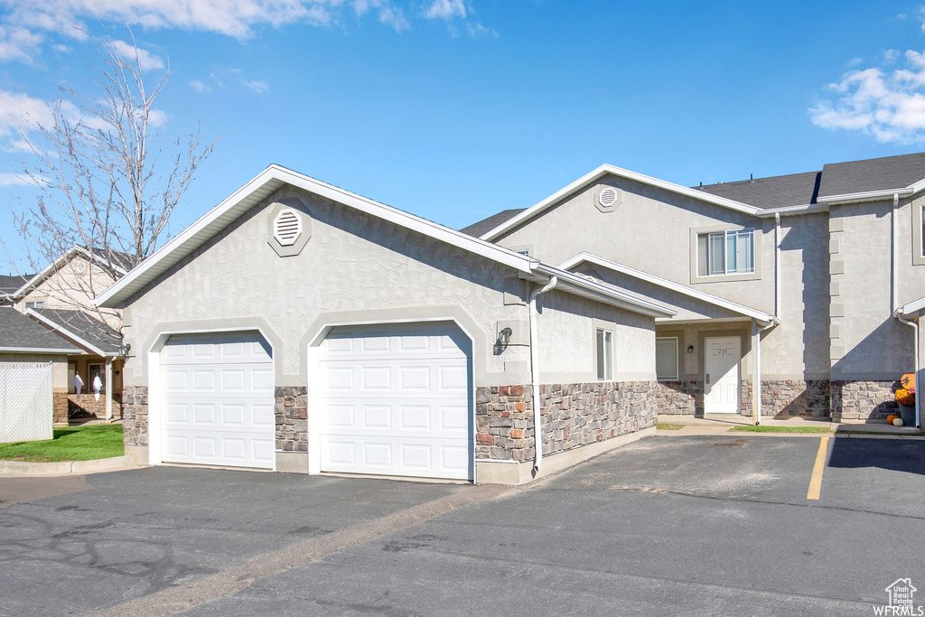 Townhome / multi-family property featuring stone siding, stucco siding, a garage, and driveway