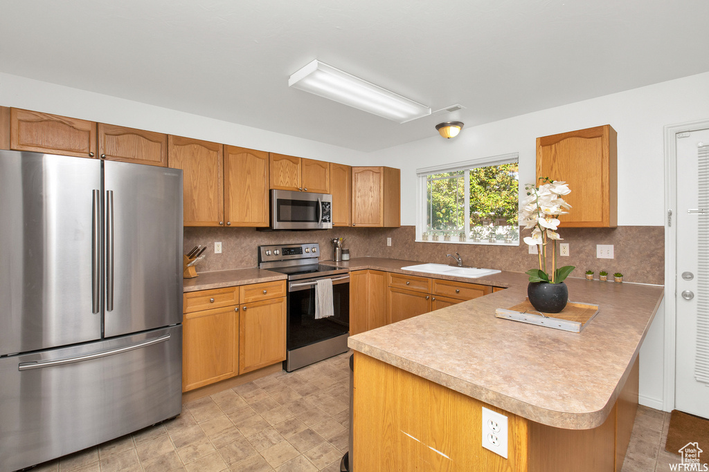 Kitchen with stainless steel appliances, a peninsula, a sink, and light countertops