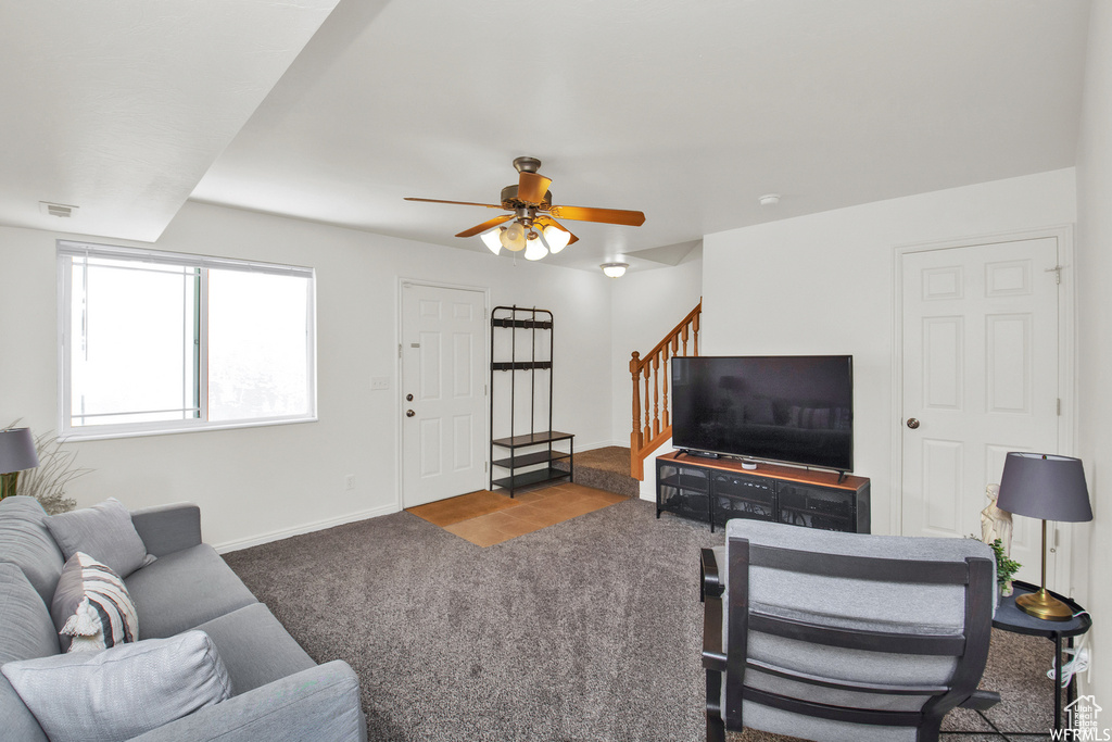 Carpeted living area featuring stairway, a ceiling fan, and baseboards