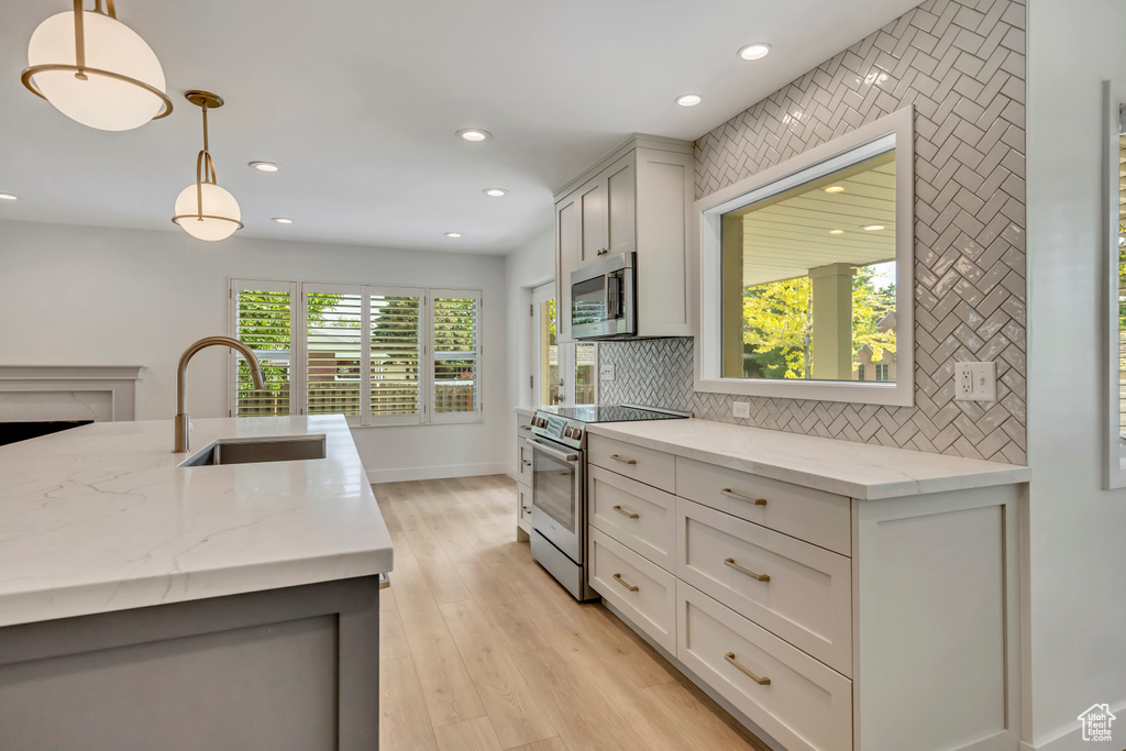 Kitchen with appliances with stainless steel finishes, recessed lighting, decorative backsplash, pendant lighting, and light wood-style floors