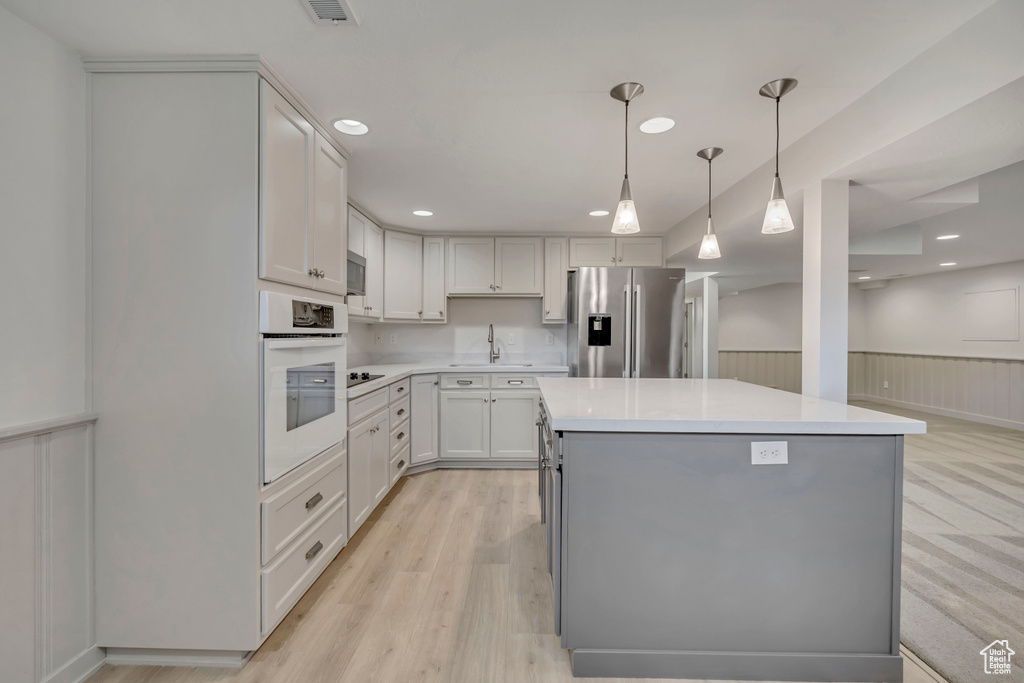 Kitchen with appliances with stainless steel finishes, wainscoting, light countertops, a kitchen island, and decorative light fixtures