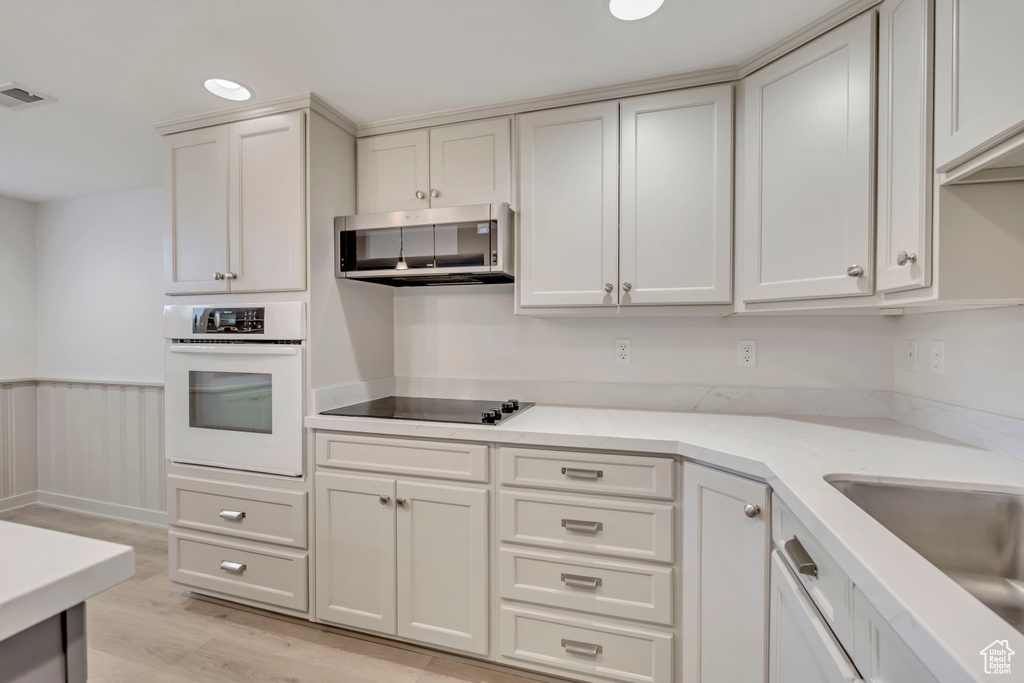 Kitchen with white oven, exhaust hood, light wood-style floors, black electric stovetop, and light stone counters
