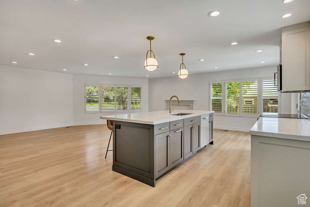 Kitchen with gray cabinets, recessed lighting, light wood finished floors, pendant lighting, and an island with sink