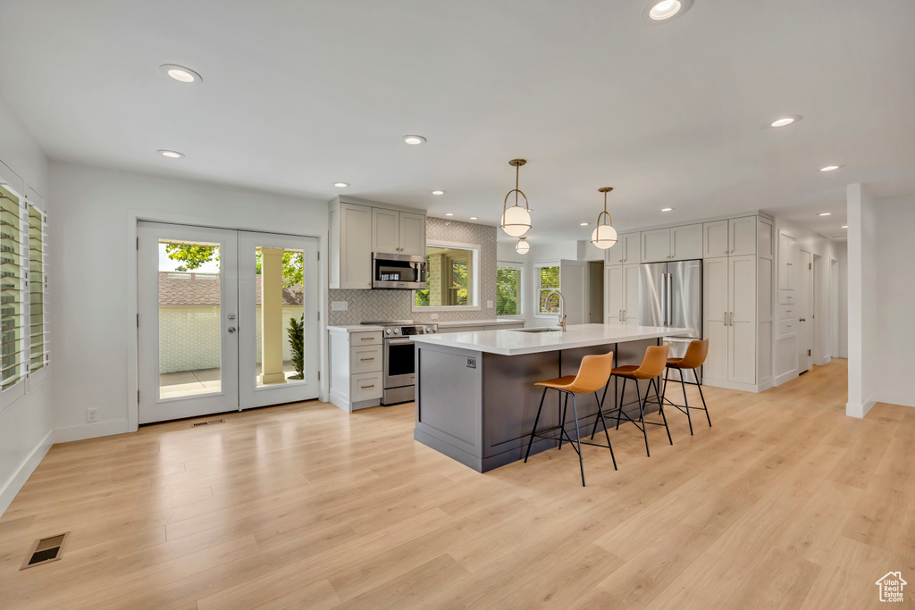 Kitchen featuring stainless steel appliances, light countertops, recessed lighting, a breakfast bar, and light wood-style flooring
