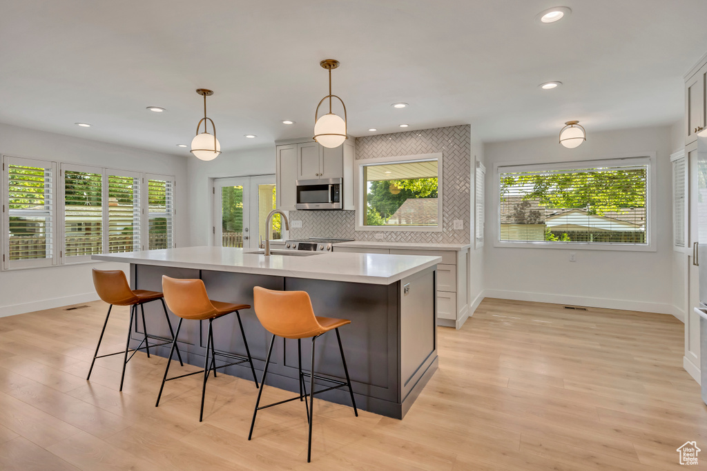 Kitchen with stainless steel microwave, light wood-style floors, light countertops, a kitchen island with sink, and a kitchen bar