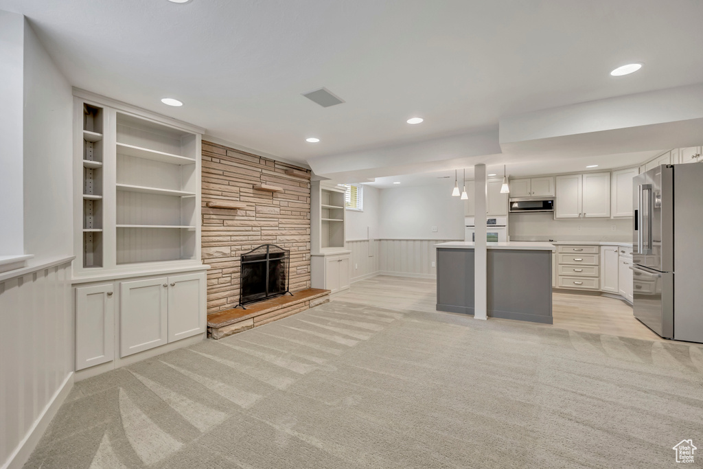 Unfurnished living room featuring light carpet, a stone fireplace, built in shelves, recessed lighting, and wainscoting