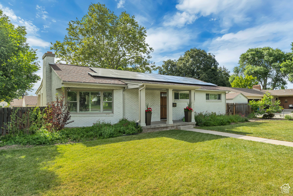 View of front of property featuring solar panels, a chimney, brick siding, covered porch, and roof with shingles